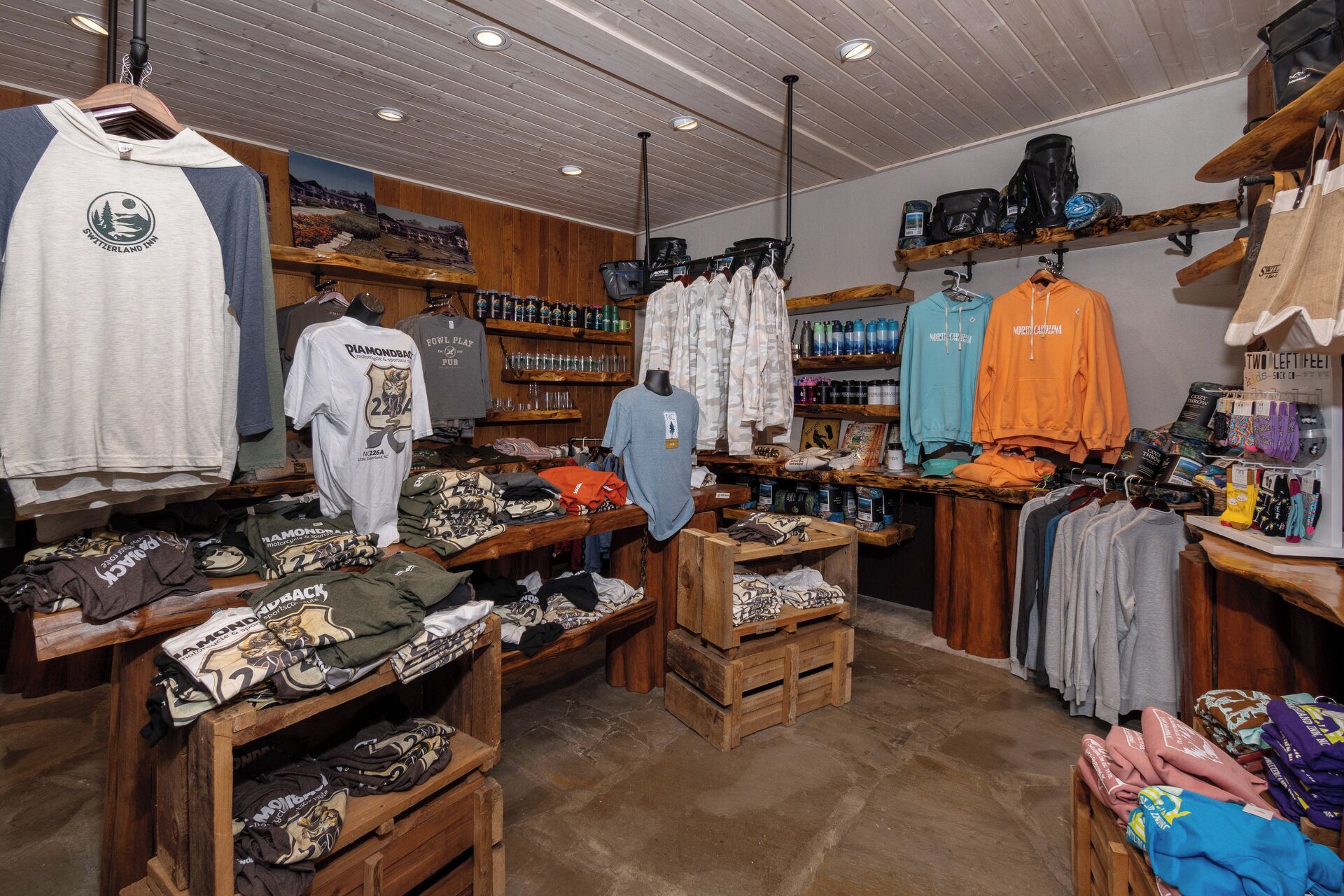 A clothing store with racks of shirts and jackets, wooden display tables, and shelves with various items.
