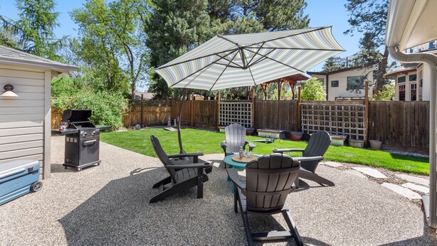 Une terrasse à l’arrière de la maison, avec un barbecue, des fauteuils Adirondack et un parasol à rayures.
