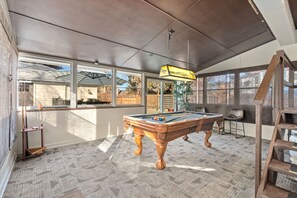 Relax and unwind in this spacious room featuring a pool table, high ceiling, and large windows.