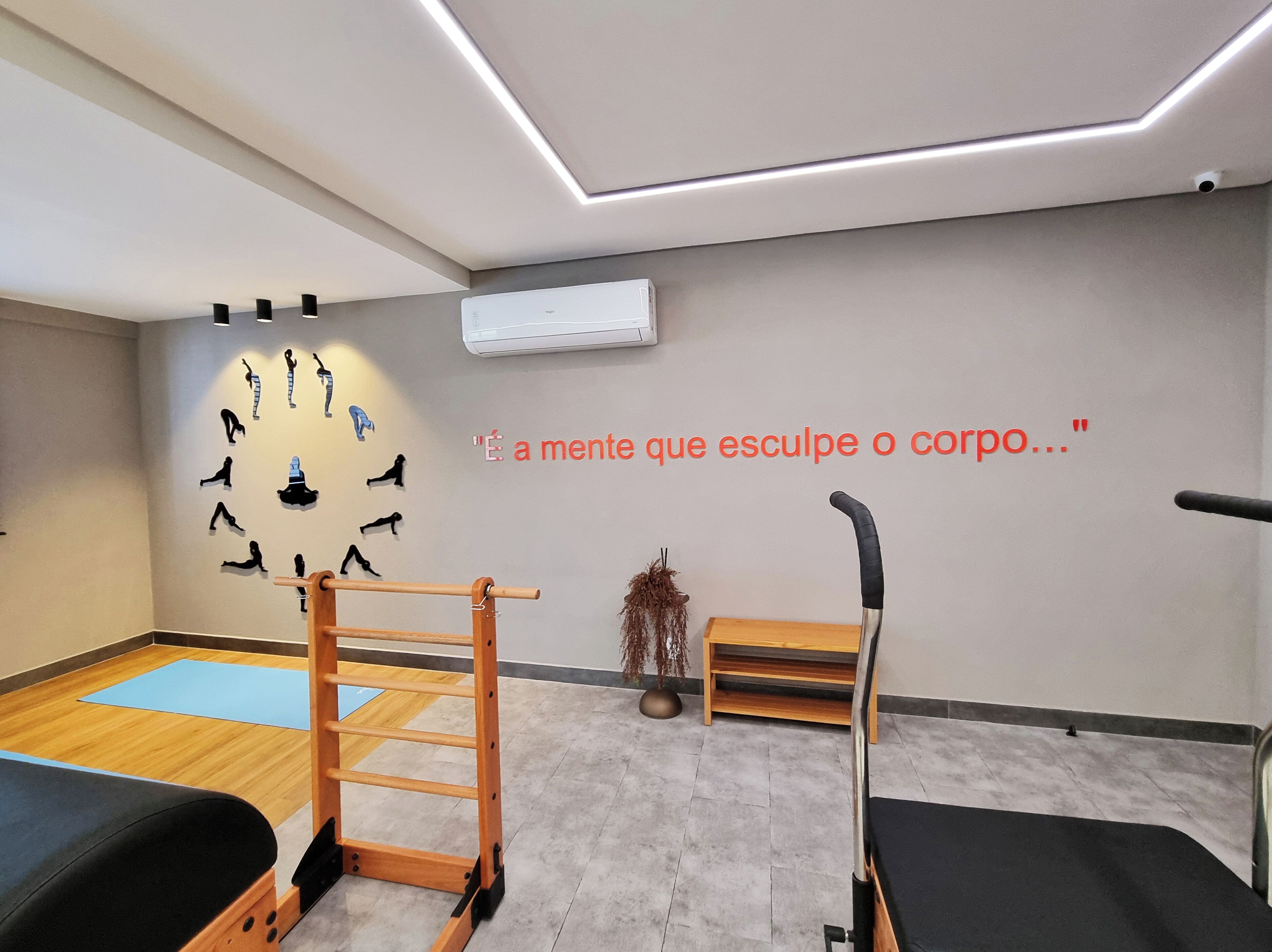 A modern therapy room with a wooden ladder, a black exercise bench, and a wall-mounted air conditioner.
