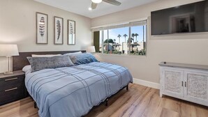 A bedroom with a bed, a ceiling fan, a TV, and a window with a view of palm trees. - BE FIRST TO STAY at The Camelback Retreat in Scottsdale (Scottsdale)