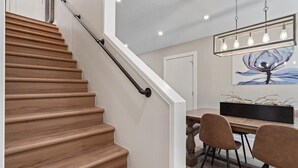 Una escalera de madera con barandilla de metal que lleva a un comedor con mesa y sillas.