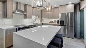 Una cocina moderna con una isla grande, electrodomésticos de acero inoxidable e iluminación colgante.