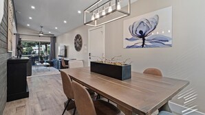 Un comedor moderno con una mesa de madera, sillas, una maceta negra y una lámpara colgante.
