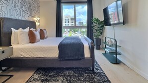 A modern hotel room with a large bed, a ceiling fan, a TV, and a view of the city.