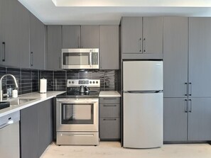 Une cuisine moderne avec des meubles gris, un four à micro-ondes, un four et un réfrigérateur en acier inoxydable.