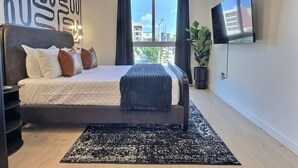 A modern bedroom with a bed, a ceiling fan, a large window with curtains, a flat-screen TV, and a potted plant. - Quiet City Getaway, Near Regions Field and Food (Birmingham)
