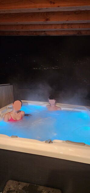 A hot tub with two people in it, surrounded by a wooden structure. - Chalet Le Criou - Morillon, Sleeps 12, Spa   (Morillon)