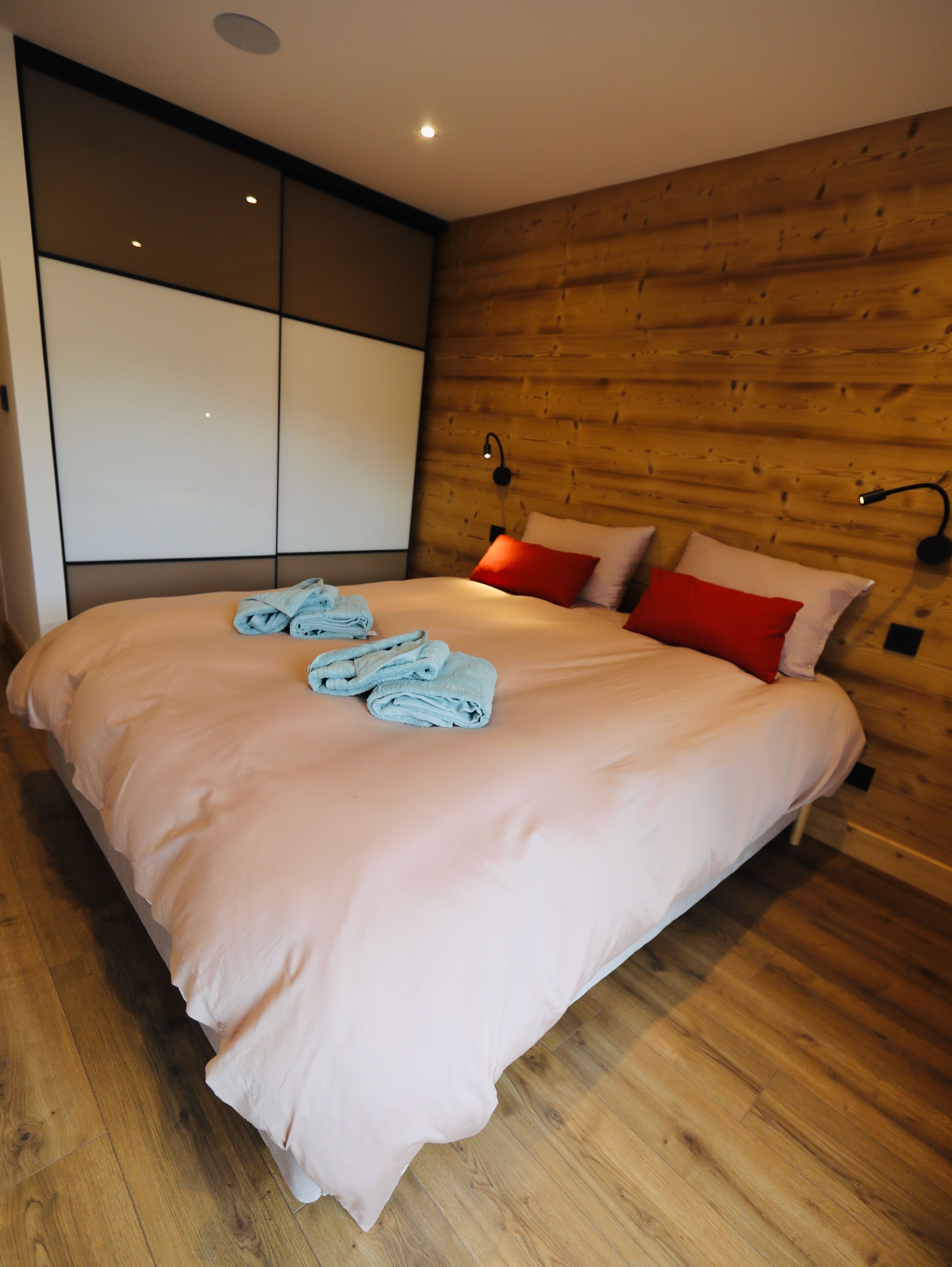 A modern bedroom with a large bed, wooden panel walls, and a built-in wardrobe.