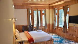 Ein Zimmer mit Holzwänden, einem Bett, einem Fernseher und großen Fenstern mit Vorhängen.