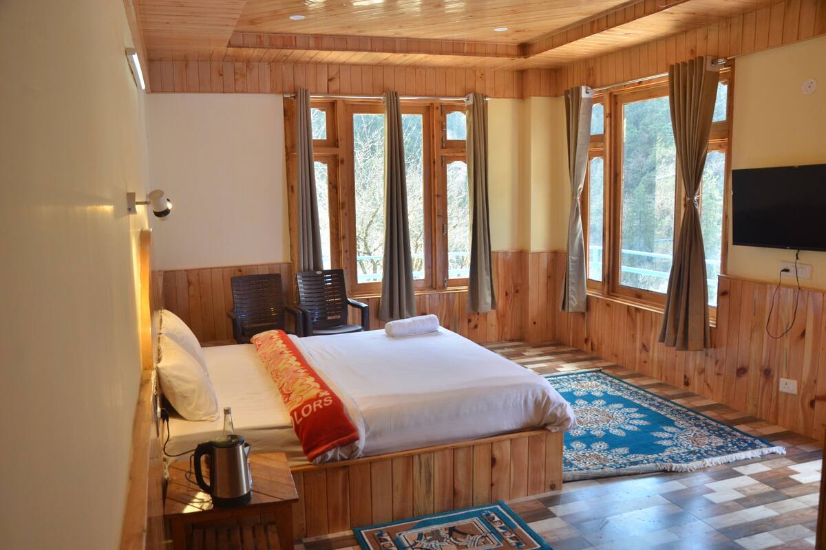 A wooden-paneled room with a bed, a television, and large windows with curtains.