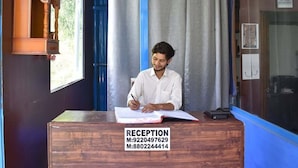 Ein Empfangsschalter mit einem Schild, das ihn als Rezeption kennzeichnet, und eine Person sitzt am Schalter und schreibt.