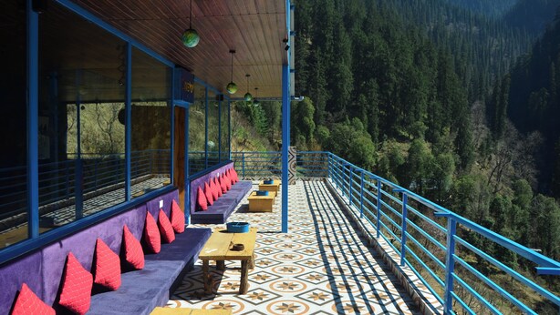 Eine Terrasse mit Holztischen und -bänken, einem gemusterten Boden und Blick auf ein bewaldetes Tal.