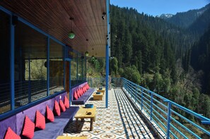 A terrace with wooden tables and benches, a patterned floor, and a view of a forested valley. - Limbo Cafe & Rooms (Banjar)