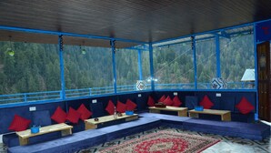 Ein Zimmer mit einem blau-roten Sofabezug, Holztischen und einem großen, gemusterten Teppich.
