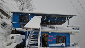 Ein zweistöckiges Gebäude mit schneebedecktem Dach und Balkon, umgeben von Schnee.