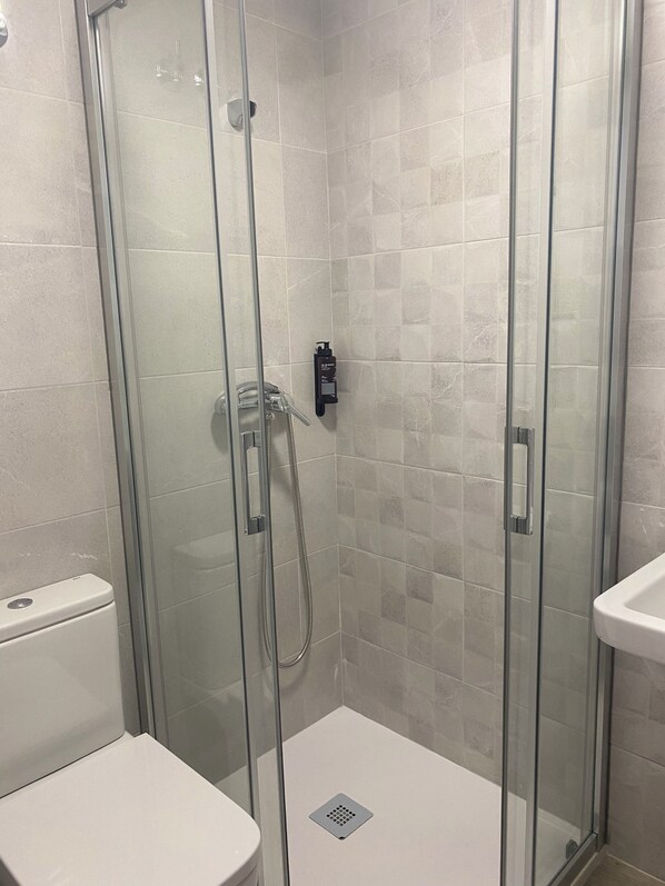 A glass-enclosed shower with a handheld showerhead and a control panel. - Albergue O Bailarín (O Barco de Valdeorras)
