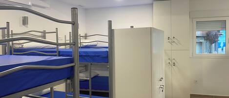 A dormitory room with bunk beds, a white wardrobe, and a window with a view of a building.