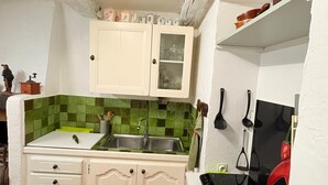 Une cuisine de taille réduite avec des meubles blancs, un dosseret de carrelage vert et une cuisinière noire.