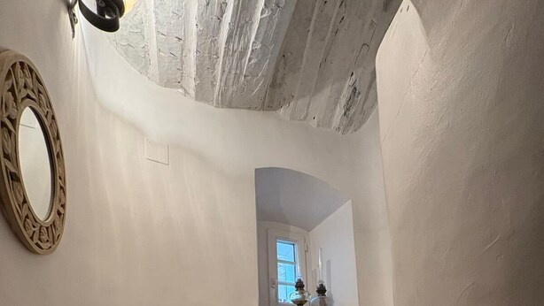 Un escalier étroit aux murs blancs, avec une petite fenêtre en haut.