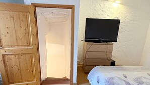 Une chambre avec une armoire en bois, un lit recouvert d’une couette à motifs floraux et un téléviseur posé sur un meuble.