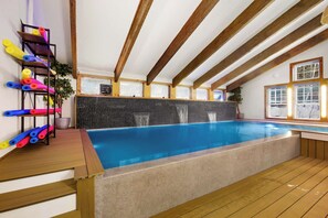Une grande piscine intérieure avec des poutres en bois et un mur recouvert de carreaux.