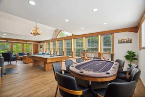 Une pièce spacieuse équipée d’une table de billard, de plusieurs chaises et d’une grande fenêtre donnant sur un paysage verdoyant.