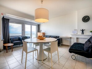 A modern living room with a round dining table, two sofas, a black armchair, a small side table, and a large window offering a view of the sea. - Renovated Apartment in Koksijde With Sea-views (Koksijde)