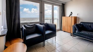 Ein modernes Wohnzimmer mit einem großen Fenster und Meerblick, einer schwarzen Ledersofa, einem Holzschrank und einem kleinen Holztisch.