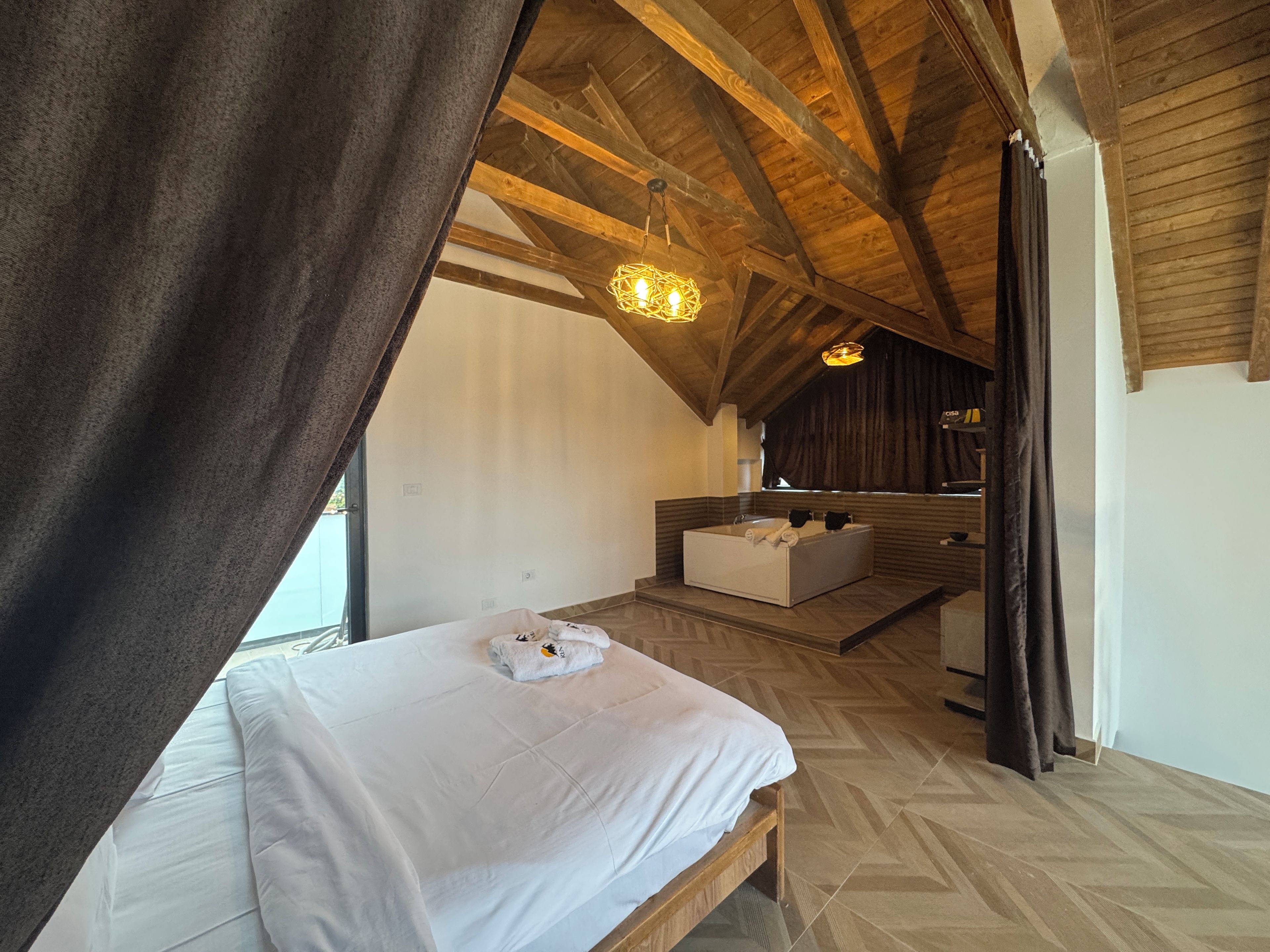 Una camera da letto con un letto grande, un angolo salotto e vista su un soffitto in legno.