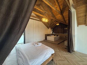 Una camera da letto con un letto grande, un angolo salotto e vista su un soffitto in legno.