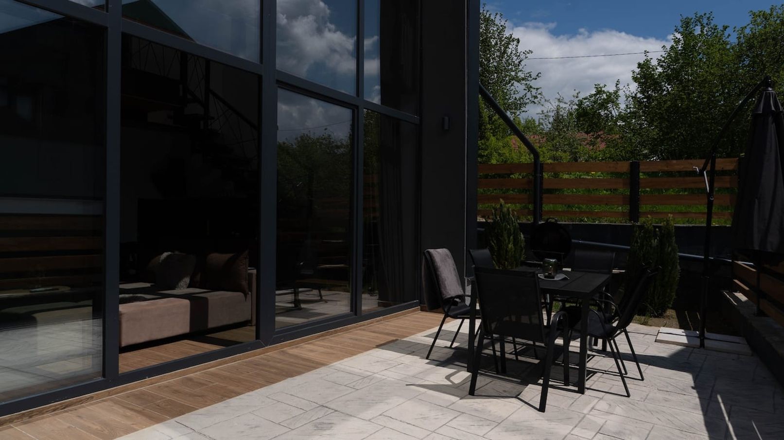 A modern outdoor patio with a dining table and chairs, a sofa, and a large glass wall.