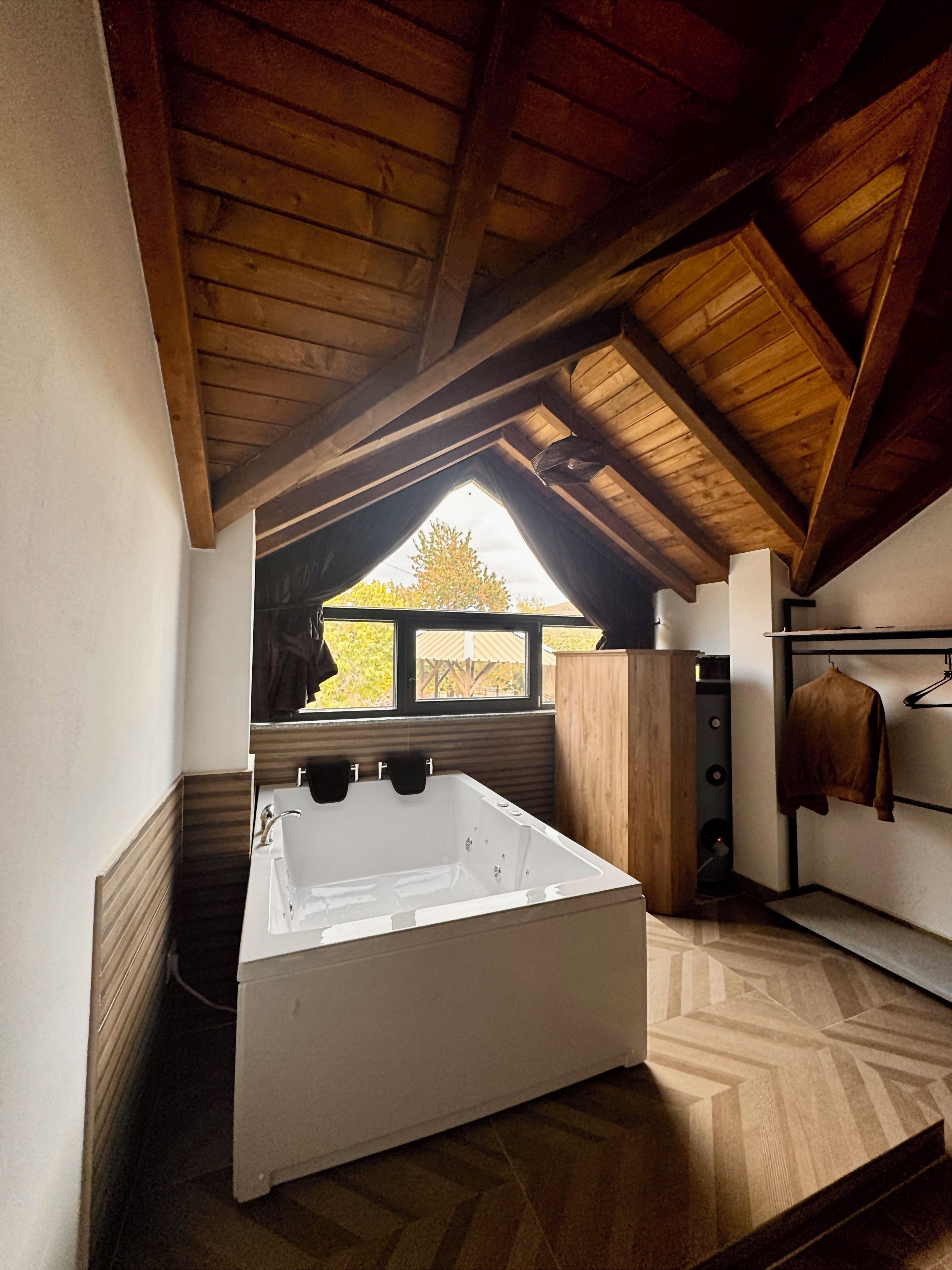 Une salle de bain moderne avec une baignoire sur pieds, des poutres en bois au plafond et une vue sur l’extérieur par une fenêtre.