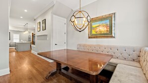 A spacious dining area with a wooden table and a cushioned bench, a pendant light, and a framed painting on the wall.