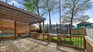 A wooden deck with railings, a covered area, and a view of a house and trees.