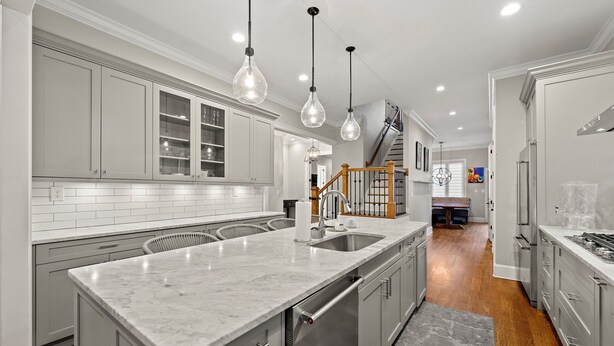 A modern kitchen with grey cabinets, a marble countertop, and stainless steel appliances.