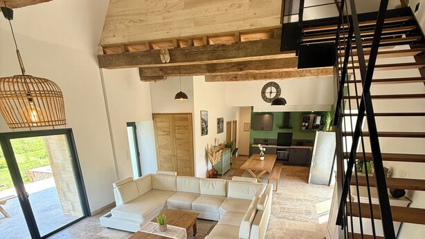 A spacious living area with a modern staircase, a dining table, and a kitchen in the background. - Charming gîte with swimming pool (Rouffignac-Saint-Cernin-de-Reilhac)