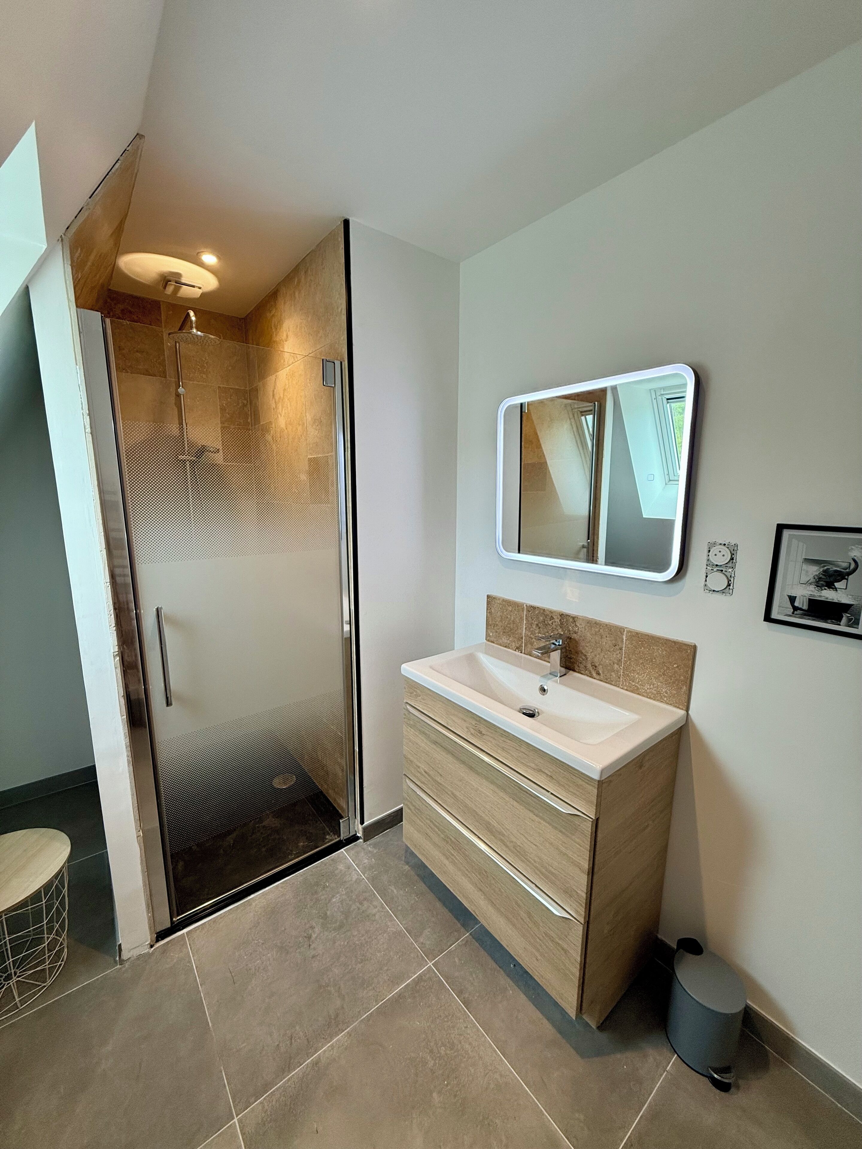 Een moderne badkamer met een douchecabine van glas, een wastafel met spiegel en een prullenbak.