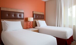 Two single beds with headboards and nightstands, each with a lamp, are set against a warm-toned wall.