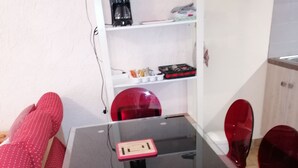 Een intieme eethoek met een glazen tafel, rode stoelen, een bank met rode stippenkussens en een witte plank met diverse voorwerpen.