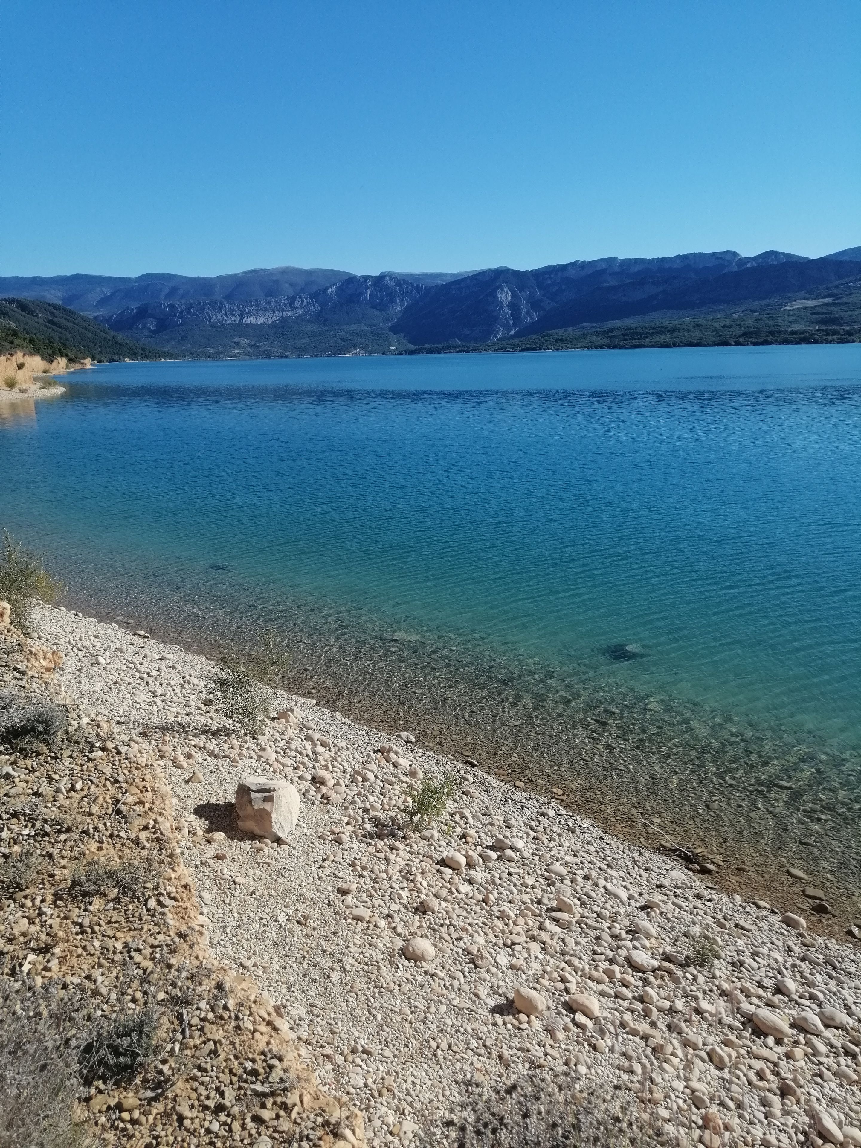 En klar sø med en klippefyldt kystlinje og bjerge i baggrunden.