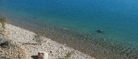 Um lago límpido com margens rochosas e montanhas ao fundo.