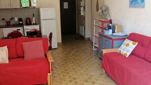 Een knus woongedeelte met een kitchenette, een eethoek en een rode bank met gestreepte kussens.