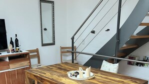 Un comedor moderno con una mesa de madera, un banco y sillas. Se ve una escalera con barandilla de metal al fondo.