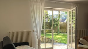 Un dormitorio con cama, una silla, un radiador y un ventanal corredera que da a un jardín.