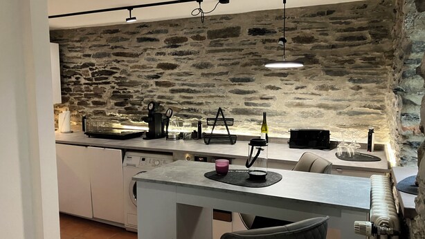 Una cocina con pared de piedra, zona de comedor con mesa y sillas, y lavavajillas empotrado.