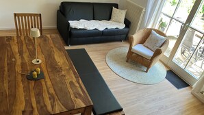 Una sala de estar moderna con una mesa de comedor de madera, un sofá negro, una silla de mimbre y un ventanal que proporciona luz natural.
