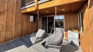 Eine Holzterrasse mit zwei Korbstühlen und einem kleinen Tisch, mit Blick auf eine verschneite Landschaft.