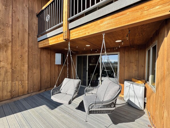 A wooden deck with two wicker chairs and a table, overlooking a building with a balcony. - Stay at the Original Feed & Grain Building on Main Street in downtown Timnath (Timnath)