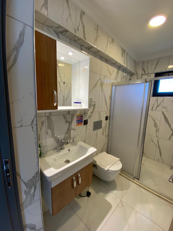 Une salle de bain moderne avec un pare-baignoire en marbre, un lavabo blanc, un meuble-lavabo en bois, des toilettes et une cabine de douche en verre.